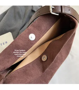Detail of the magnetic buckle closure on a brown suede bucket bag with leather strap