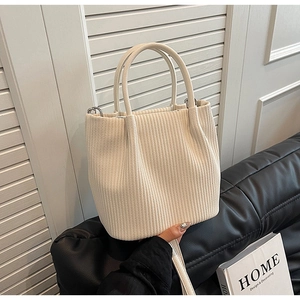 Detail view of cream pleated bucket bag with textured vertical stripes on a leather sofa