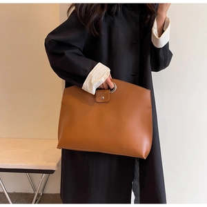 Detail of caramel brown tote bag featuring a round metal handle and ORIGINALLY logo