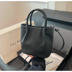 Detail of black pleated bucket bag with leather handles and adjustable shoulder strap