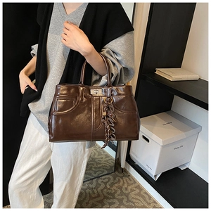 Detail of deep brown glossy leather tote bag with metal lock and fringe tassel charm