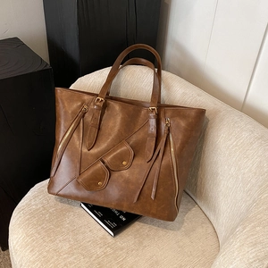 Brown vintage PU leather tote bag with asymmetric pockets and tassel detail on a chair