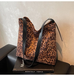 Detail view of large leopard print tote bag with black leather straps on a sofa