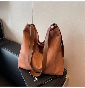 Detailed texture of a caramel brown suede hobo bag on a black leather seat background