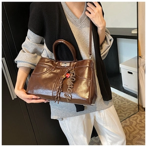 Detail view of brown glossy tote bag featuring unique denim pocket stitching and silver clasp
