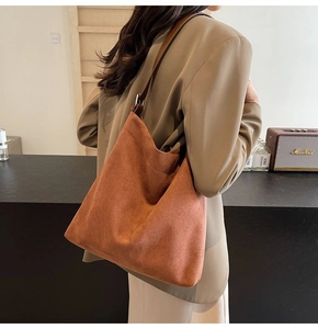 Detail view of a large caramel suede hobo bag worn over the shoulder in a warm indoor setting