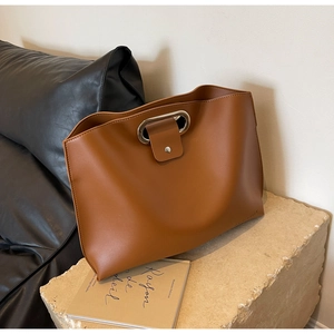 Detail of a brown leather tote bag with a sleek silver oval metal handle and snap closure