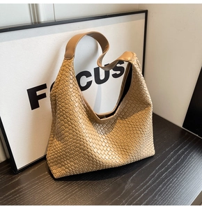 Close-up of khaki woven leather hobo shoulder bag on a black wooden surface