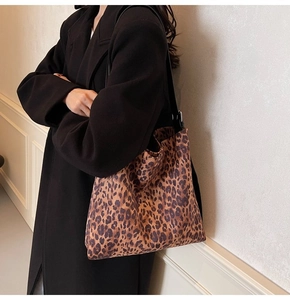 Close-up of leopard print tote bag with black straps worn over a long black coat