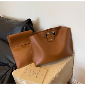 Brown leather tote bag set on stone surface with a matching inner envelope pouch