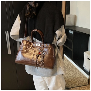 Detail of dark brown glossy patent leather tote bag with vintage metal turn-lock and charms