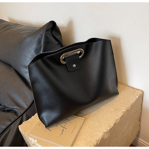 Minimalist black leather handbag with oval metal handle on a stone pedestal