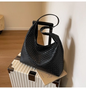 Close-up of black woven leather tote bag leaning on a white suitcase in a lifestyle setting