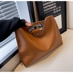 Macro view of minimalist brown large tote with oval metal handle and debossed text detail