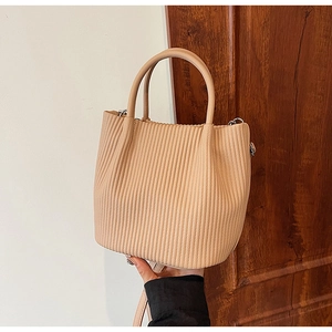 Detail of nude pleated bucket bag showing vertical embossed texture and dual handles