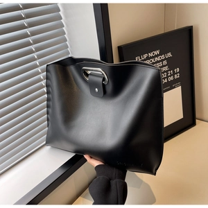 Close-up of minimalist black leather tote bag with metal hollow handle and snap closure