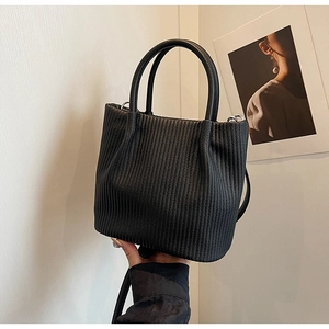 Detail of black pleated bucket bag with vertical textures and versatile double handles