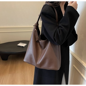 Detail of a large brown pebbled leather tote bag worn with a black coat in a modern interior