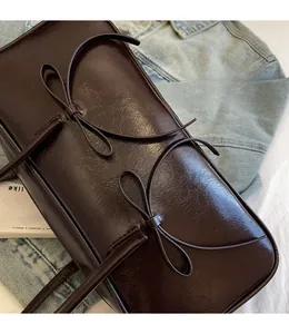 Detailed shot of dark brown glossy leather bag with decorative bows on denim jacket