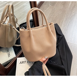 Detail view of beige pleated bucket bag with dual handles and detachable shoulder strap