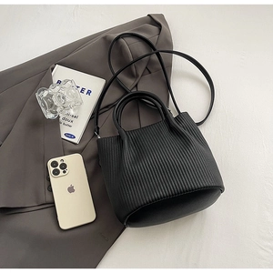 Detail of black pleated bucket bag with cylinder handles on minimalist office setting