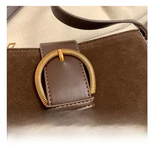 Close-up of matte brown shoulder bag with a textured golden circular metal buckle detail