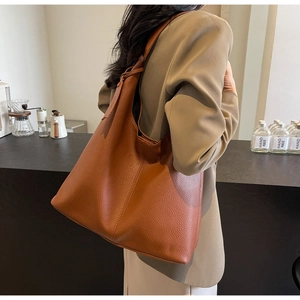 Close-up of brown lychee texture leather hobo bag worn by model in a minimalist cafe