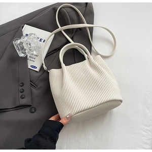 Close-up of a pleated beige bucket bag with smooth handle and textured faux leather detail