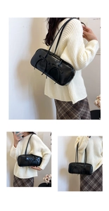 Detail of black patent leather underarm bag featuring decorative ribbon bows on the front