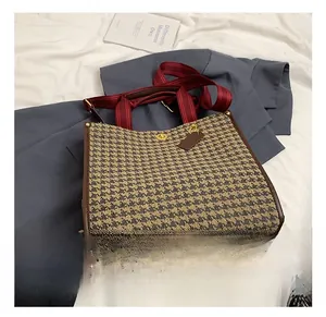 Close-up of houndstooth tote bag with brown leather trim and striped shoulder strap