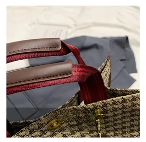 Close-up of brown leather handles and striped webbing on a houndstooth tote bag