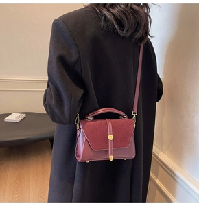 Burgundy crossbody bag with matte and suede texture shown on a model in a black coat