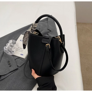 Detail of black lychee leather bucket bag with silk scarf on handle and crossbody strap