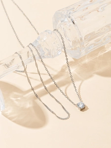 Detail of layered stainless steel necklace featuring a round prong-set cubic zirconia pendant