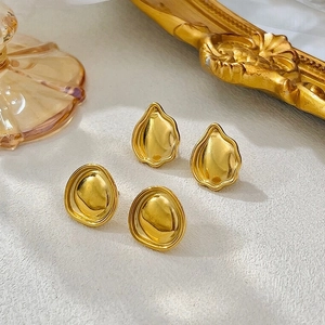 Détail macro de boucles d'oreilles irrégulières en acier doré sur surface en pierre
