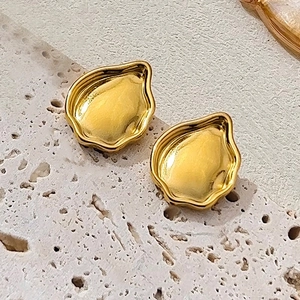 Détail des boucles d'oreilles irrégulières en métal doré sur pierre travertin