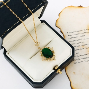 Vintage emerald style oval pendant necklace with gold floral border on a blue jewelry box