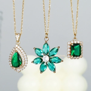 Three emerald green crystal necklaces with teardrop and floral pendants in gold finish