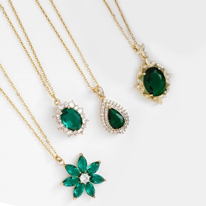 Four vintage emerald pendant necklaces in gold settings with halo diamond accents