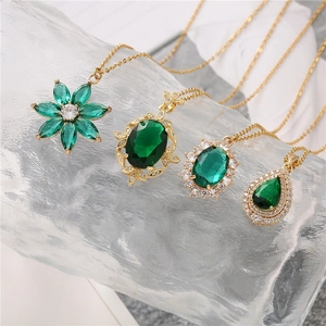 Four green crystal necklaces with gold floral and teardrop pendants on a glass base