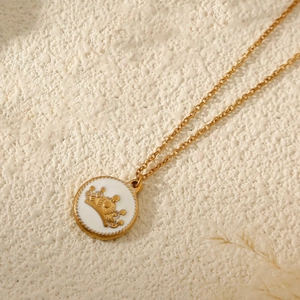 French vintage gold necklace with white enamel crown pendant on a white stone background