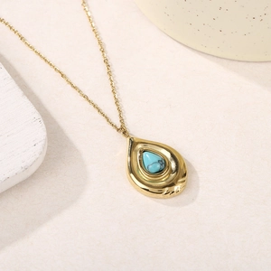 Détail macro du pendentif en turquoise goutte sur une chaîne en acier doré