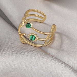Gros plan d'une bague dorée soleil et lune avec malachite verte sur fond en soie