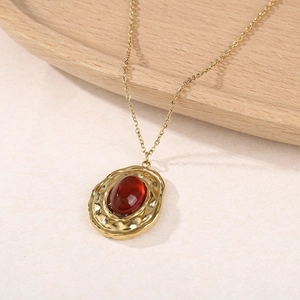 Détail d'un collier doré vintage avec pierre rouge foncée et pendentif martelé