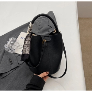 Detail of black pebbled leather bucket bag with decorative scarf and gold hardware