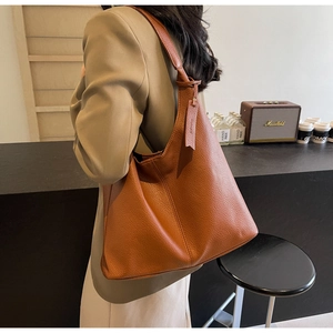 Brown lychee leather hobo bag with wide shoulder strap shown in a trendy urban cafe setting