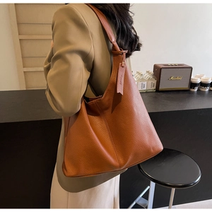 Brown leather tote bag on shoulder showing large capacity and lychee texture