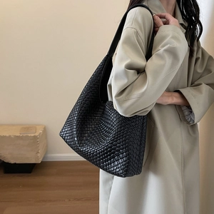 Large black woven leather tote bag shown on model with minimalist commuter outfit