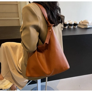 Brown lychee leather tote bag shown on a model in a stylish coffee shop setting