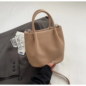 Close-up of beige pleated bucket bag with round handle and silver metal hardware details